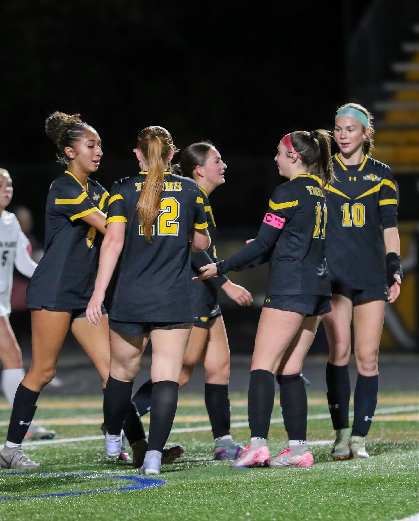 Soccer team celebrates on field in black uniforms with yellow accents.