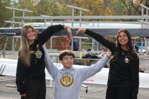Three happy people forming the letter M with their arms at a rowing event.