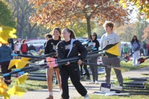 Rowing team carrying oars at a park during autumn, preparing for a practice session.