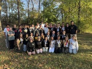 Group of students with medals posing outdoors in a sunny park setting, celebrating an achievement.