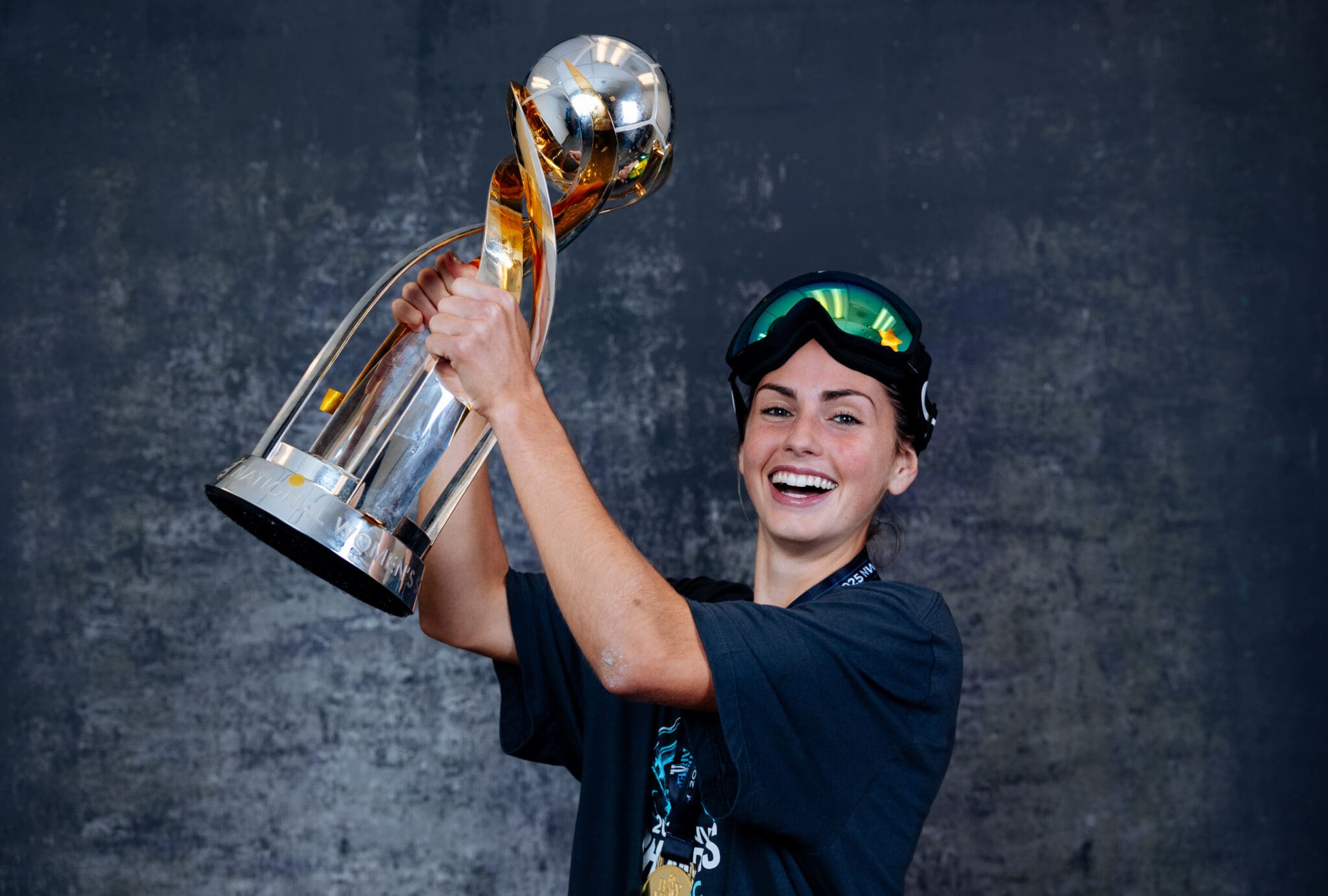 Smiling athlete with trophy in ski goggles celebrates victory in winter sports competition.