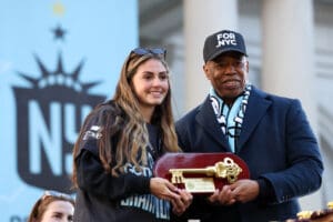 Two people holding a ceremonial key at a public event, with a light blue background featuring the NYC logo.