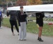 Rowing team carrying boat on riverside path, autumn trees in background.