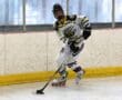 Roller hockey player in action on rink, wearing a white and yellow jersey, focusing on the puck.