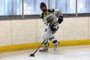 Roller hockey player in action on rink, wearing a white and yellow jersey, focusing on the puck.