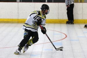 Inline hockey player in motion, wearing white jersey, holding a hockey stick, focused on the puck on the rink.
