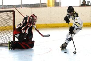Roller hockey player in white attempts shot against goalie in black during an indoor game.