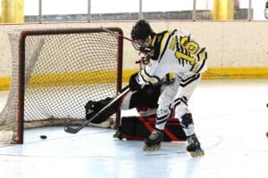 Roller hockey player attempts to score against goalie in dynamic match action.