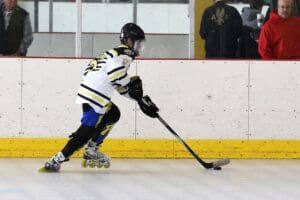 Inline hockey player in action, wearing protective gear, skating with puck on indoor rink.