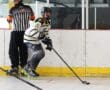 Roller hockey player in action on rink, wearing black and white gear, referee nearby.