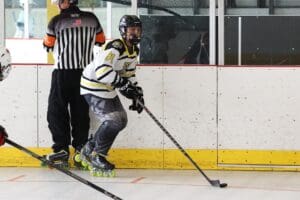 Roller hockey player in action on rink, wearing black and white gear, referee nearby.
