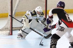 Roller hockey goalie defends against player approaching with puck, on rink.