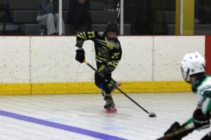 Hockey player in action on rink, wearing black jersey number 27, skates forward with stick.