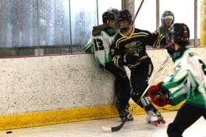 Ice hockey game action with players in black and green jerseys, close-up rink battle near boards.