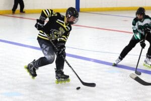 Two roller hockey players in action on an indoor rink, one nearing the puck, wearing protective gear.