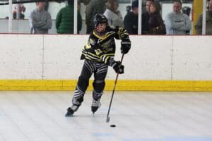 Youth inline hockey player in action, focused on puck control during a match on the rink.