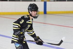 Young ice hockey player in black and yellow gear poised with a stick on the rink.