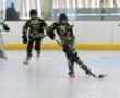 Youth roller hockey game with players in action, wearing black and green jerseys on an indoor rink.