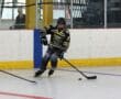 Inline hockey player in black and yellow gear skates on a rink, controlling the puck with a stick.