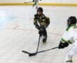 Two inline hockey players compete for the puck on a rink, one in black and yellow and the other in white and green.
