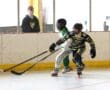 Youth ice hockey players in action during a competitive game, with spectators watching from the sidelines.