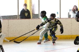 Youth ice hockey players in action during a competitive game, with spectators watching from the sidelines.
