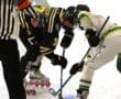 Roller hockey players face-off as referee watches, wearing team jerseys and gear on the rink.