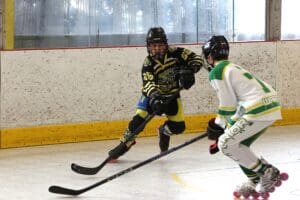 Two youth hockey players in action on an indoor rink, one in black and yellow, the other in green and white.