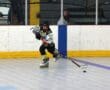 Roller hockey player in black and yellow uniform taking a shot on an indoor rink.