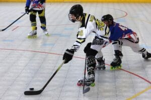 Roller hockey players in action, wearing colorful uniforms and gear during an intense game on an indoor rink.