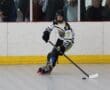 Young inline hockey player in action on the rink, focusing on the puck with spectators in the background.