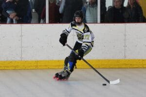 Young inline hockey player in action on the rink, focusing on the puck with spectators in the background.