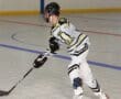 Roller hockey player in action on indoor rink, wearing black and yellow jersey, holding a hockey stick.