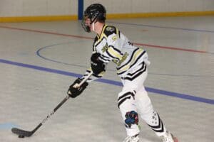 Roller hockey player in action on indoor rink, wearing black and yellow jersey, holding a hockey stick.
