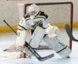 Hockey goalie in action, guarding the net during a game on an indoor rink. Sports equipment visible.