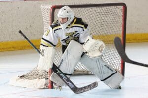 Hockey goalie in action, guarding the net during a game on an indoor rink. Sports equipment visible.