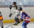 Two inline hockey players in action during a match, referee observing on the rink.