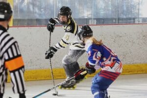 Two inline hockey players in action during a match, referee observing on the rink.