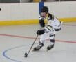 Inline hockey player in action dribbling puck on rink, wearing white and black uniform.