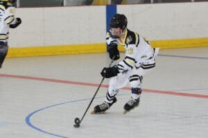 Inline hockey player in action dribbling puck on rink, wearing white and black uniform.