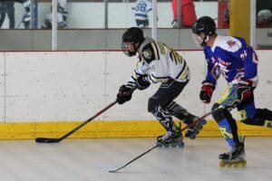 Two roller hockey players compete intensely on an indoor rink.
