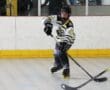 Youth roller hockey player in action on the rink, wearing a black and white jersey and inline skates.