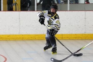 Youth roller hockey player in action on the rink, wearing a black and white jersey and inline skates.