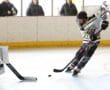 Hockey player in action on the rink with goalie ready, spectators watching from behind the barrier.