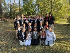 Group of young athletes posing outdoors with medals, celebrating achievements in a wooded park setting.