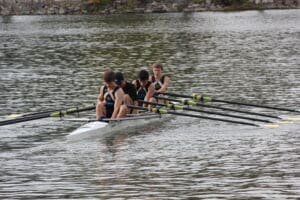 Four-person rowing team competing on a calm river with synchronized oars and sporting uniforms.