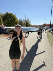 Rowing team member carrying a boat on a sunny day, preparing for practice or a race.