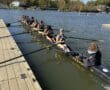 Rowing team prepares to launch on a sunny day by the dock, surrounded by scenic autumn foliage.