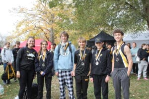 Group of rowers with medals smiling at a fall event, surrounded by people and trees.