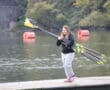 Woman carrying rowing oars on dock by the lake with orange buoys in the background.